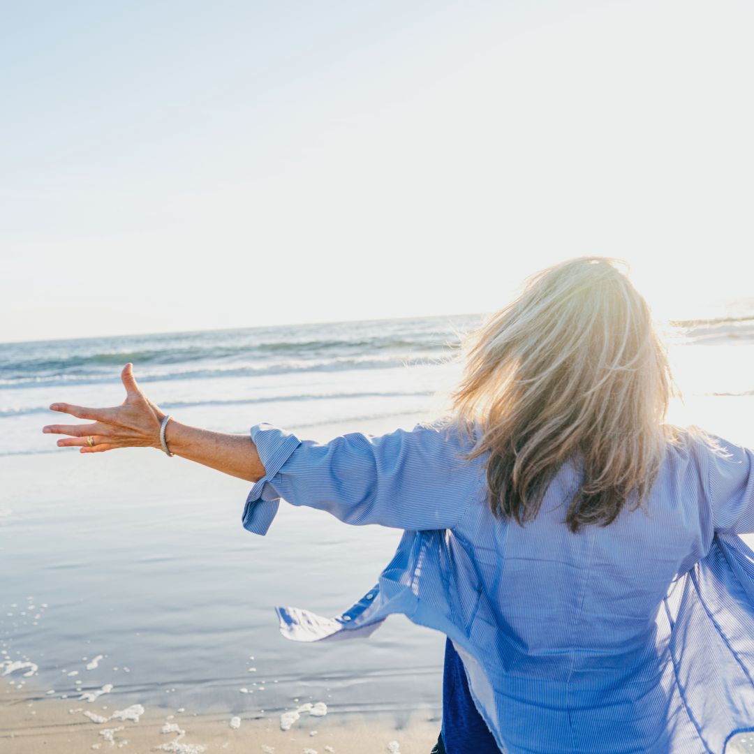 woman in blue shirt arms open at the beach